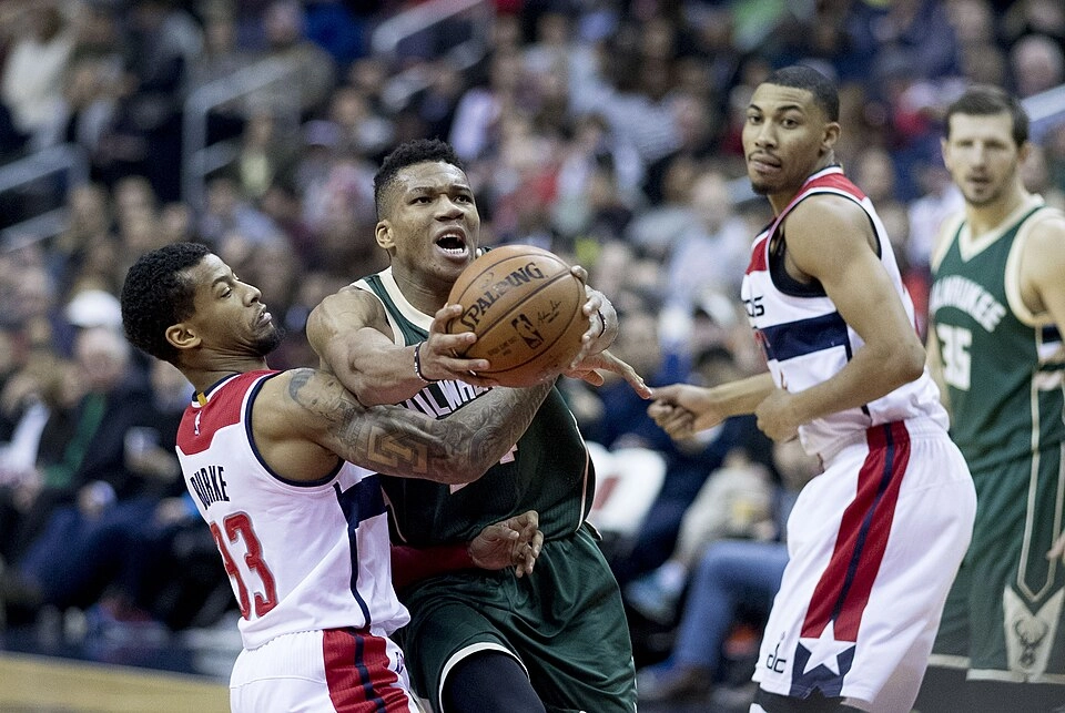 公鹿看板球星 Giannis Antetokounmpo 身穿深綠色客場球衣強力切入禁區，遭巫師隊防守者纏鬥（攝影：Keith Allison，授權 CC BY-SA 2.0，來源 Wikimedia Commons）