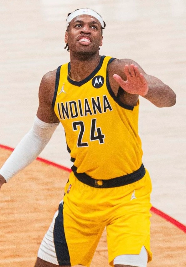 Buddy Hield 身穿印第安那溜馬黃色 24 號球衣，於 NBA 比賽場上抬頭望向籃框、右手伸出的動作（攝影 All-Pro Reels，授權 CC BY-SA 2.0，來源 Wikimedia Commons）