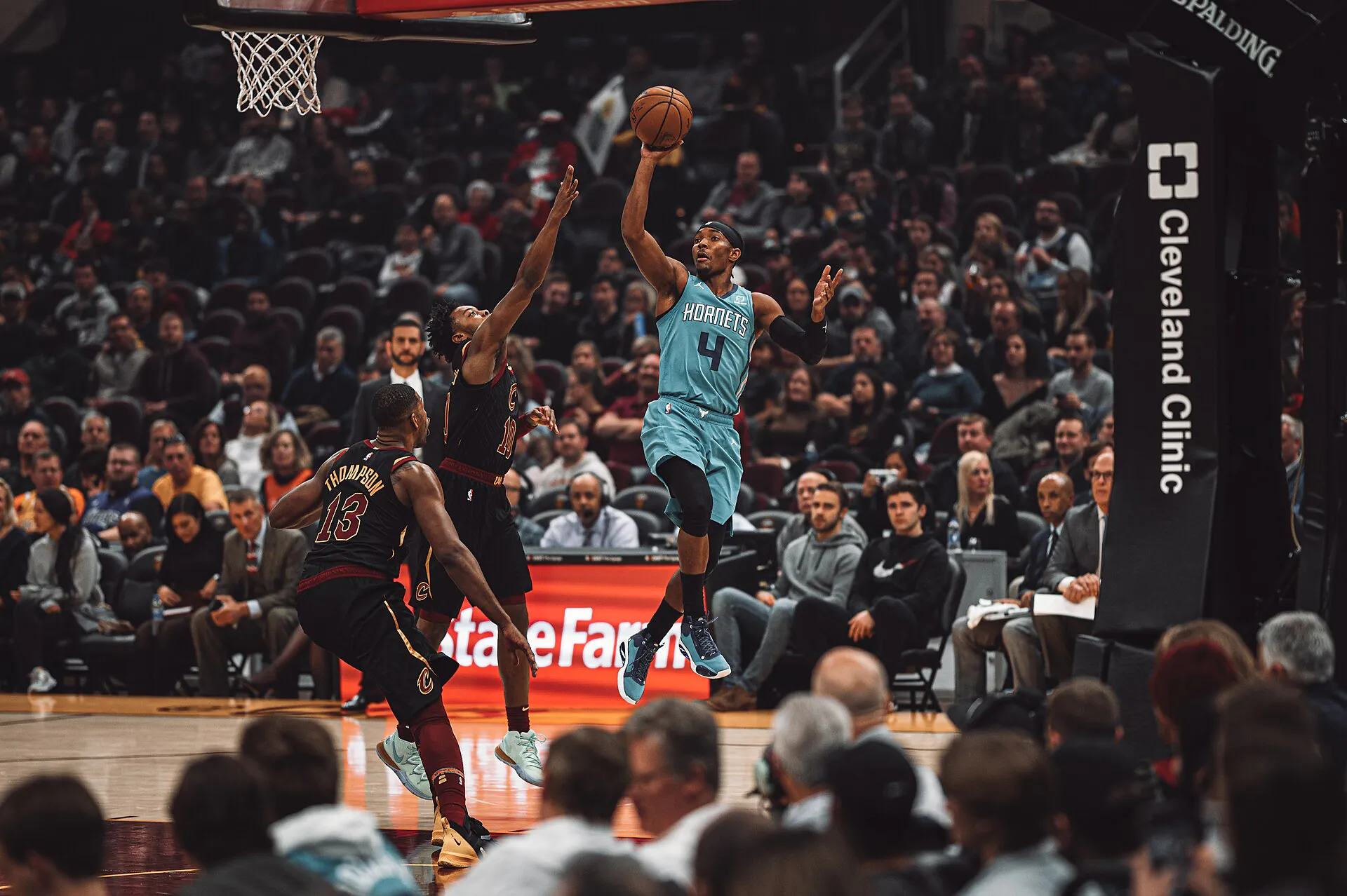 夏洛特黃蜂 4 號後衛身穿藍綠色客場球衣，在克里夫蘭騎士 Tristan Thompson 等人防守下於籃下拋投出手（攝影 Erik Drost，授權 CC BY 2.0，來源 Wikimedia Commons）