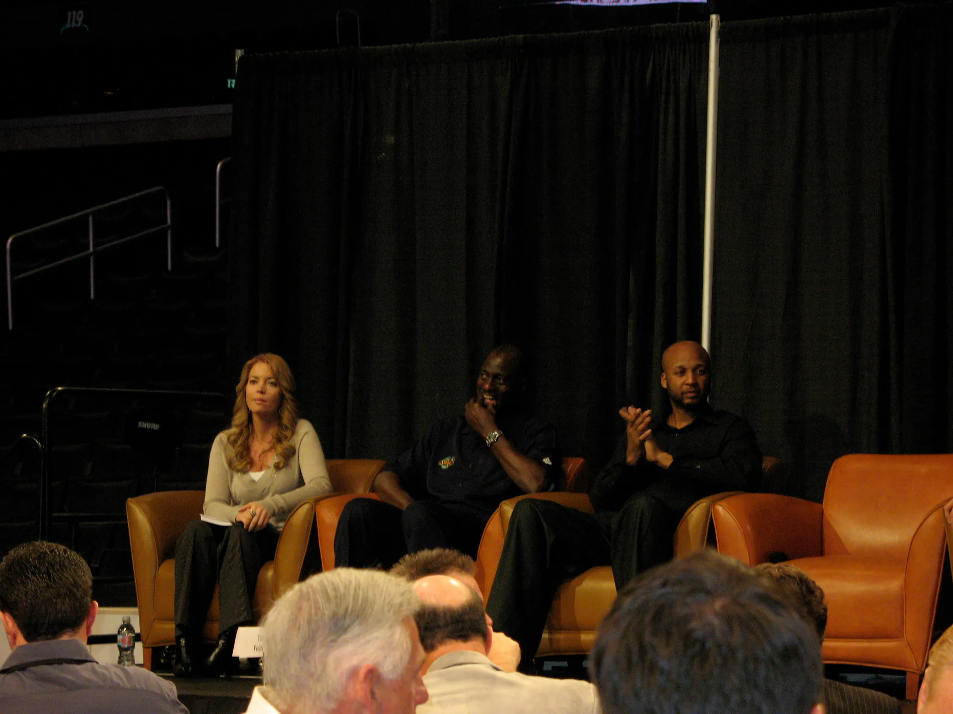 2009 年 1 月 Jeanie Buss 與湖人名宿 Michael Cooper、Brian Shaw 坐在台上的皮椅出席活動，攝影 donielle，CC BY-SA 2.0，Wikimedia Commons