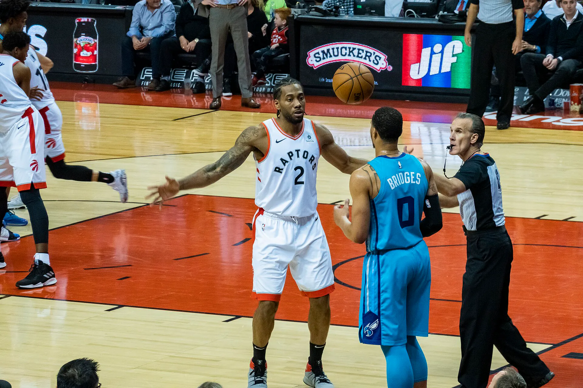 Kawhi Leonard 身穿暴龍白色 2 號球衣，在多倫多主場張開雙臂防守黃蜂 0 號 Miles Bridges，右側為吹哨的裁判（攝影 Chensiyuan，授權 CC BY-SA 4.0，來源 Wikimedia Commons）