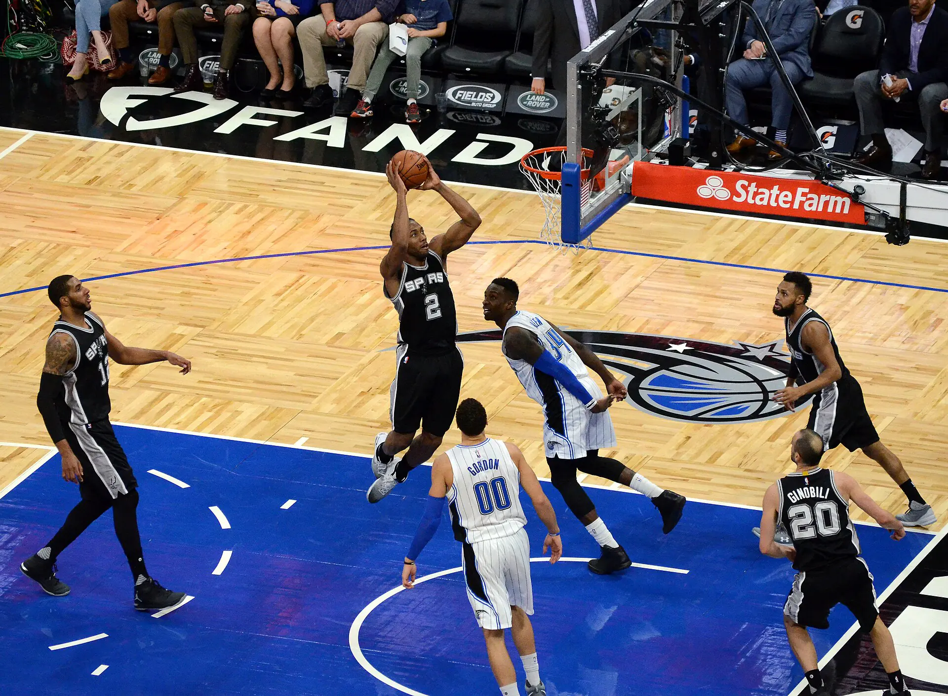 Kawhi Leonard 身穿馬刺黑色 2 號球衣在禁區附近跳起雙手出手，魔術 00 號 Aaron Gordon 與 34 號球員防守，馬刺 12 號與 20 號隊友在旁（攝影 Jose Garcia，授權 CC BY 2.0，來源 Wikimedia Commons）