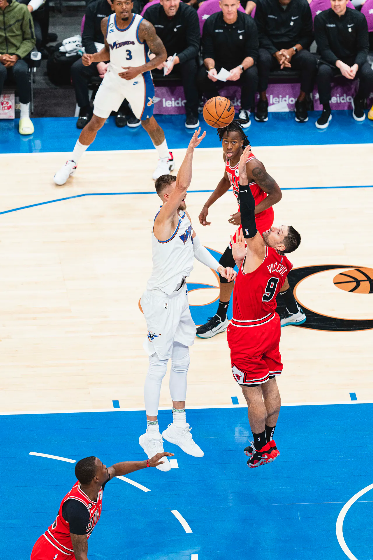 Kristaps Porzingis 身穿巫師白色球衣跳起出手，公牛 9 號 Nikola Vucevic 伸手封阻，後方為巫師 3 號 Bradley Beal（攝影 All-Pro Reels，授權 CC BY-SA 2.0，來源 Wikimedia Commons）