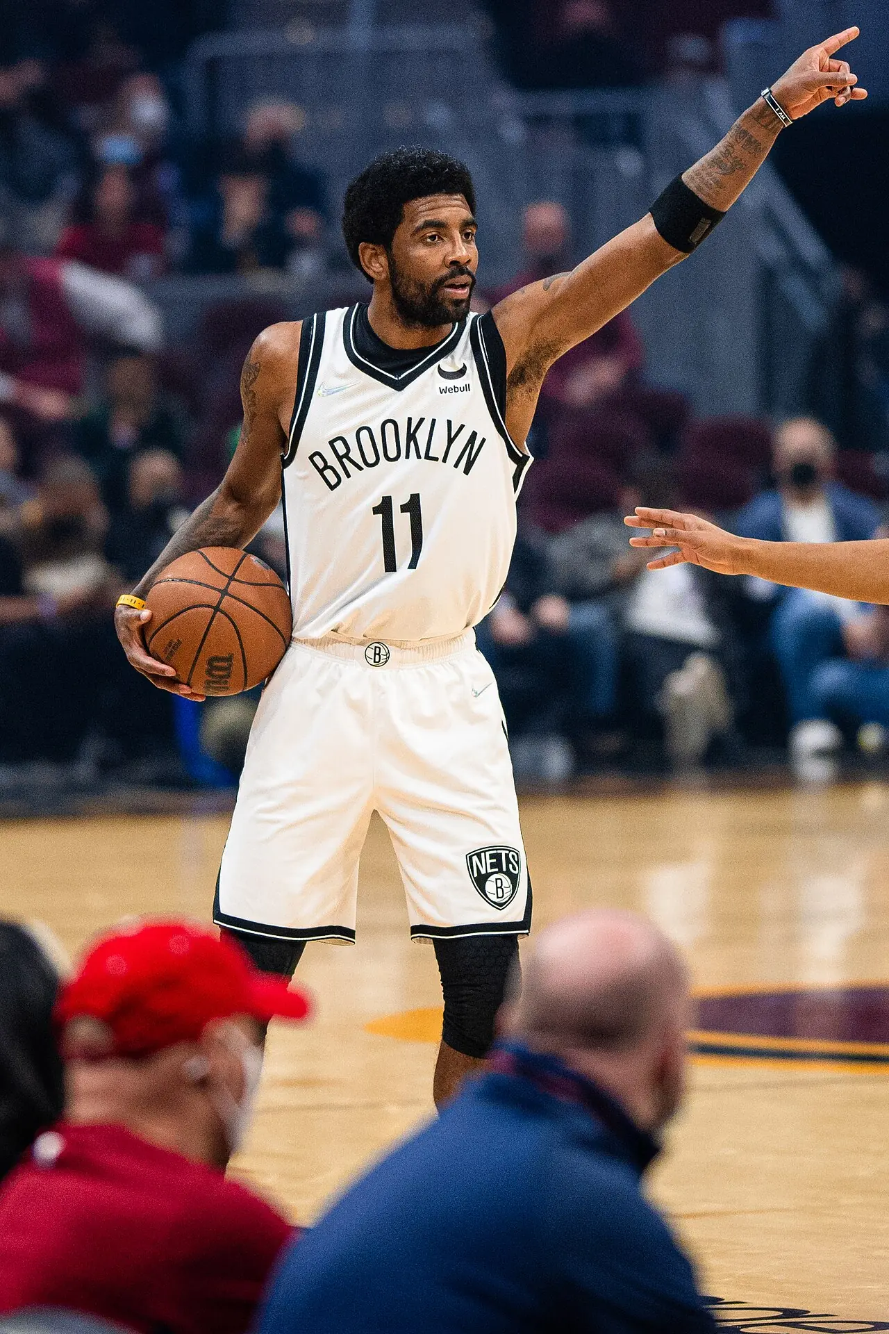 Kyrie Irving 身穿布魯克林籃網 11 號白色球衣，左手持球、右手舉起指揮進攻。攝影 Erik Drost，授權 CC BY 2.0，來源 Wikimedia Commons