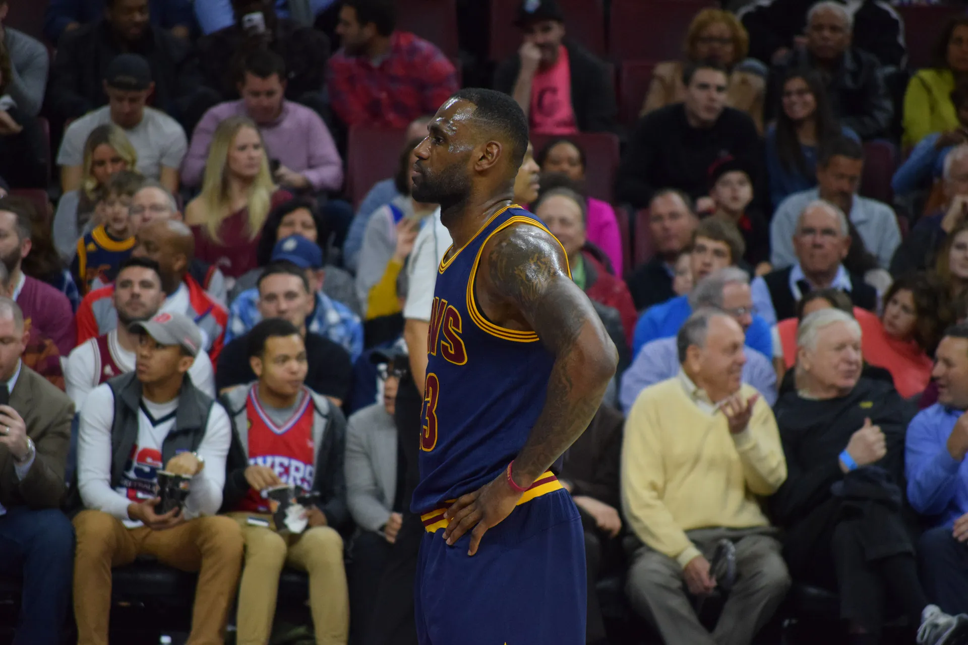 身穿騎士深藍色 23 號球衣的 LeBron James 在費城客場雙手叉腰站在場邊，後方看台有身穿 76 人球衣的球迷