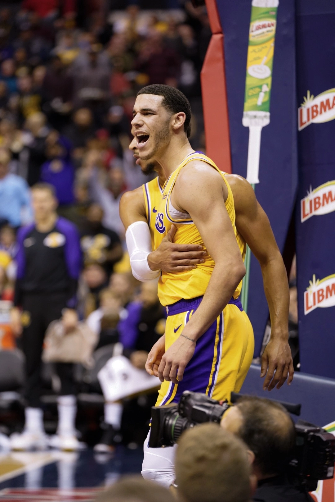 Lonzo Ball 身穿洛杉磯湖人金色球衣，於籃架旁張口吶喊情緒激動，隊友在旁攔抱。攝影：All-Pro Reels，CC BY-SA 2.0 授權，來源 Wikimedia Commons。