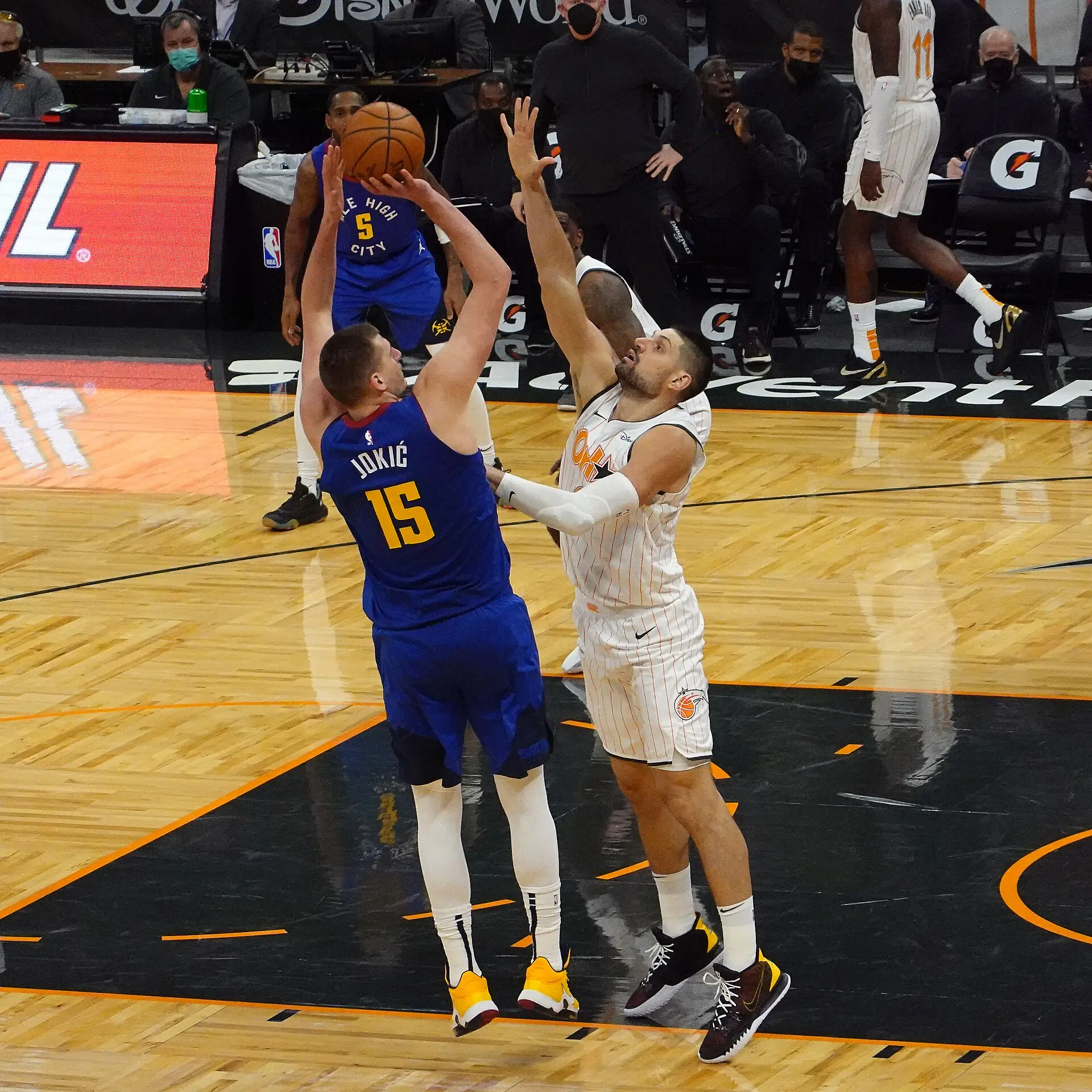 Nikola Jokic 身穿金塊藍色 15 號球衣，在魔術 Nikola Vucevic 伸手防守下出手投籃（攝影 Jose Garcia，授權 CC BY-SA 2.0，來源 Wikimedia Commons）