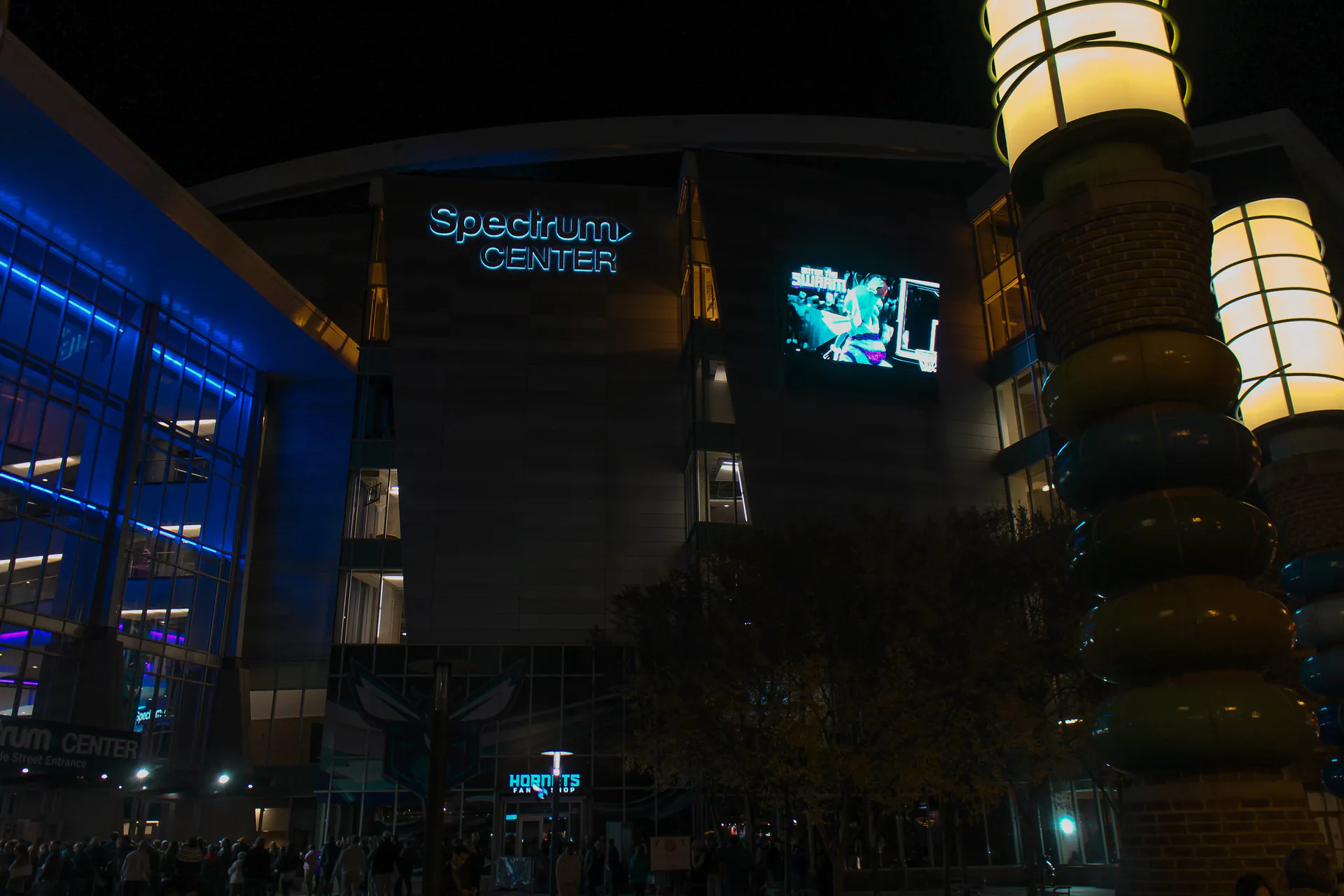 夜間的夏洛特 Spectrum Center 外觀，大螢幕播放黃蜂畫面，入口處聚集球迷
