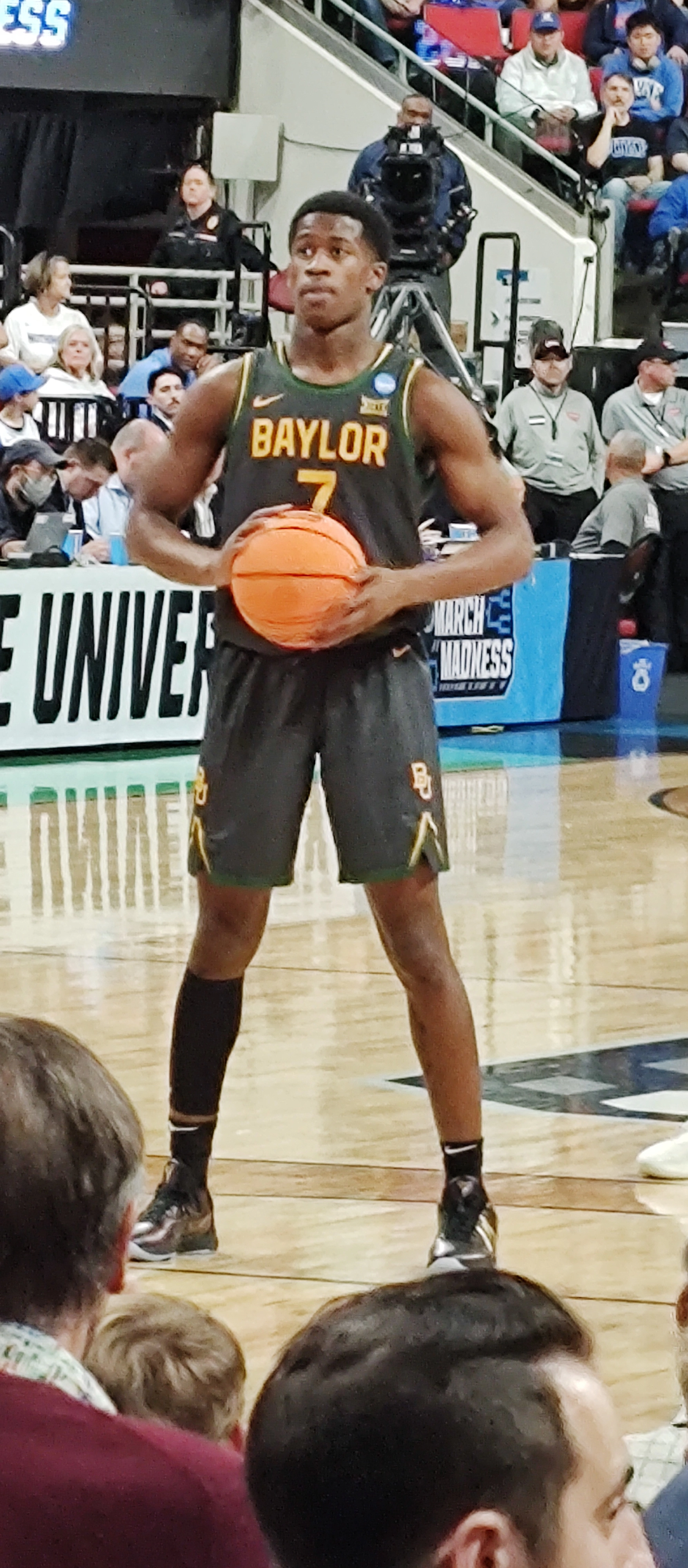 VJ Edgecombe 身穿 7 號 Baylor 黑綠色球衣，在 NCAA 錦標賽比賽中持球。攝影：SneakinDeacon，授權 CC BY-SA 2.0，來源 Wikimedia Commons。