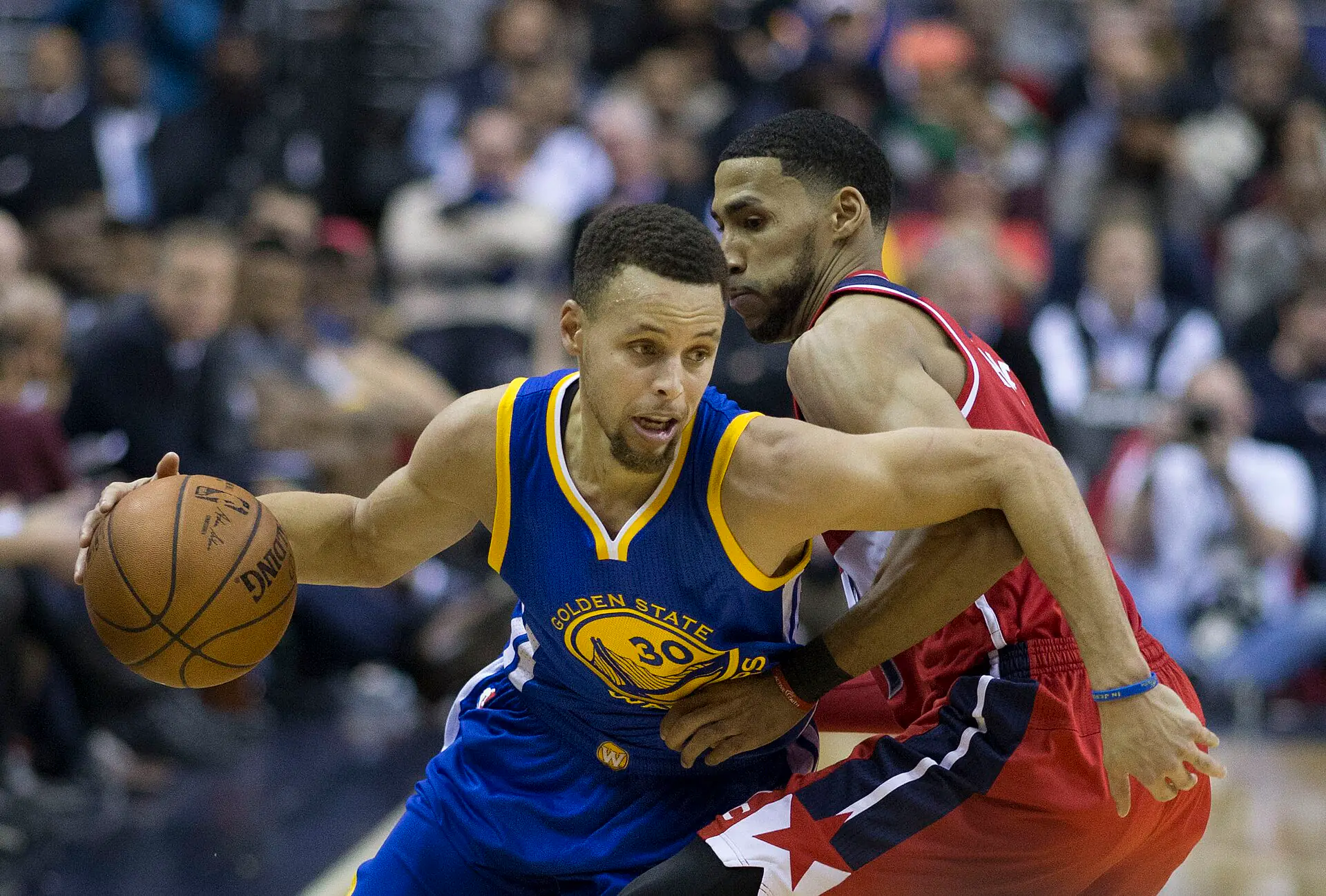 勇士 30 號 Stephen Curry 身穿藍色球衣運球突破，巫師 Garrett Temple 貼身防守（攝影 Keith Allison，授權 CC BY-SA 2.0，來源 Wikimedia Commons）