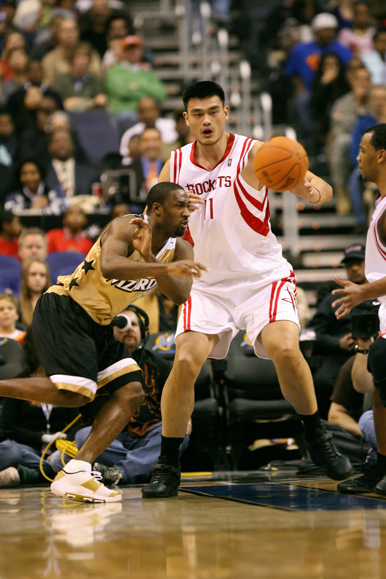 2006 年火箭 Yao Ming 高位持球、巫師 Gilbert Arenas 從身前切過，攝影 Keith Allison，CC BY-SA 2.0