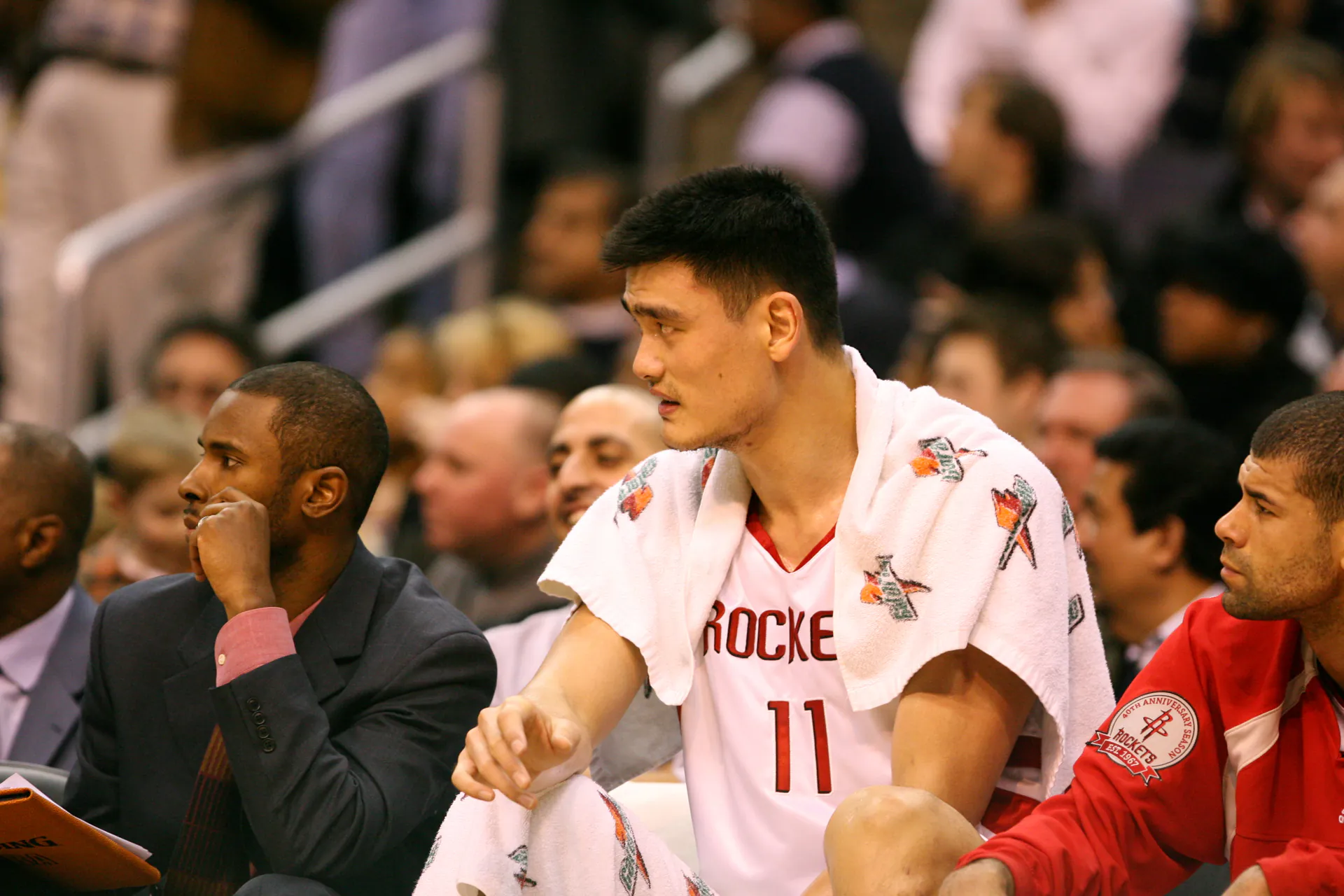 2006 年火箭 Yao Ming 披著毛巾坐在板凳席觀戰，攝影 Keith Allison，CC BY-SA 2.0